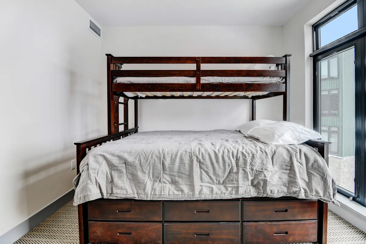 A cozy bedroom with a twin-over-queen bunk bed and a larger bed features built-in storage drawers beneath. The space is welcoming, practical for groups or families, and perfect for kids or friends.