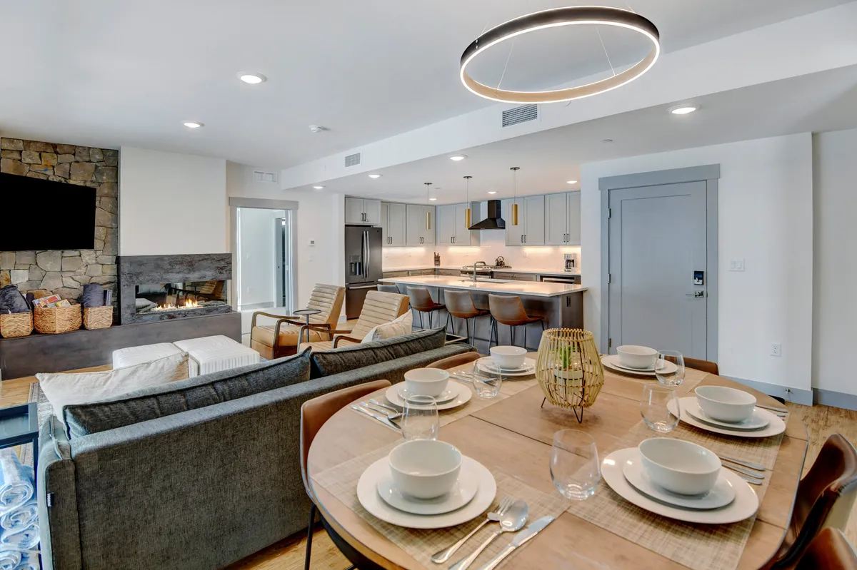 A welcoming interior that frames a modern kitchen equipped with sleek appliances, a dining table set for guests, and a cozy seating area by a fireplace. The space is warm and tastefully decorated, embodying the atmosphere of togetherness and celebration.