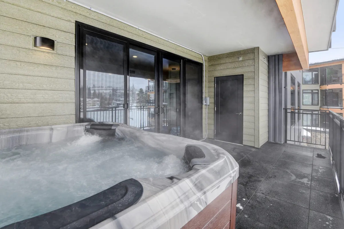 An inviting outdoor hot tub set on a spacious patio, framed by large glass doors and surrounded by serene natural views. The setting exudes tranquility and relaxation, hinting at rejuvenation after a day of adventure.