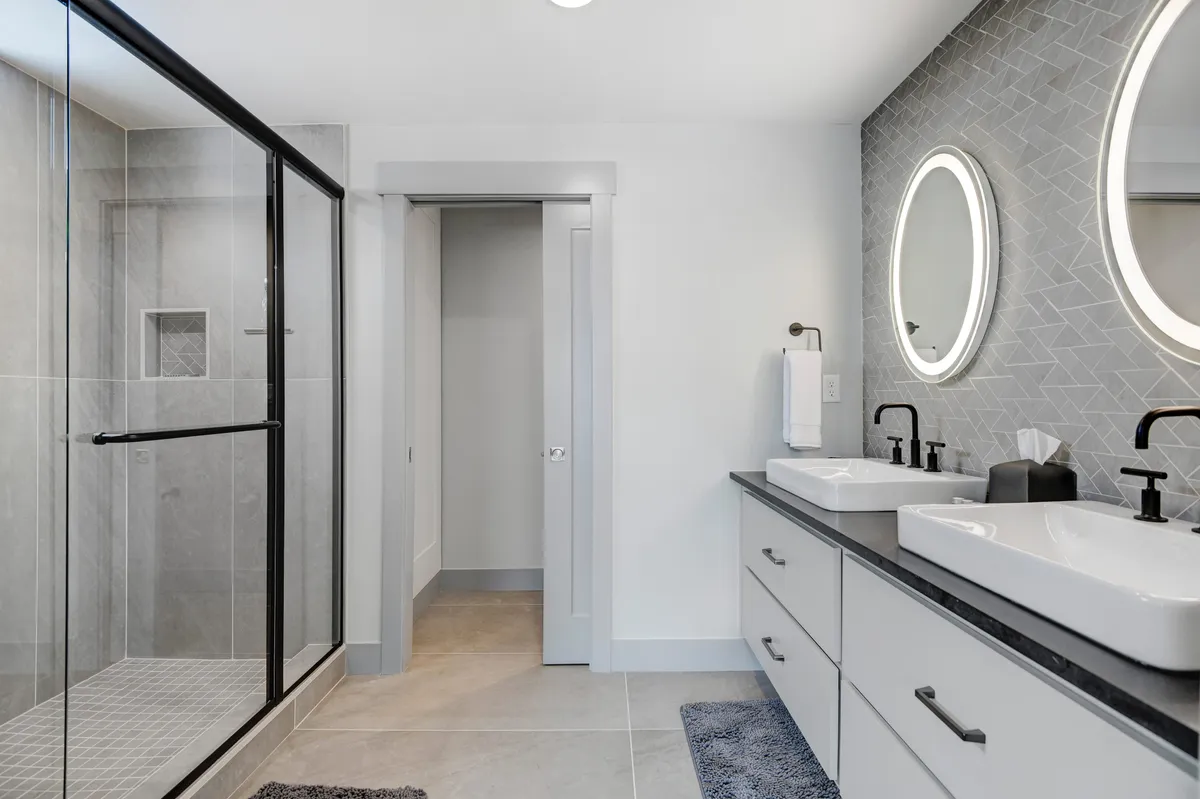 A contemporary bathroom with double sinks, circular mirrors, a glass shower enclosure, and striking hexagonal tilework creates a spa-like environment ideal for self-care and relaxation.