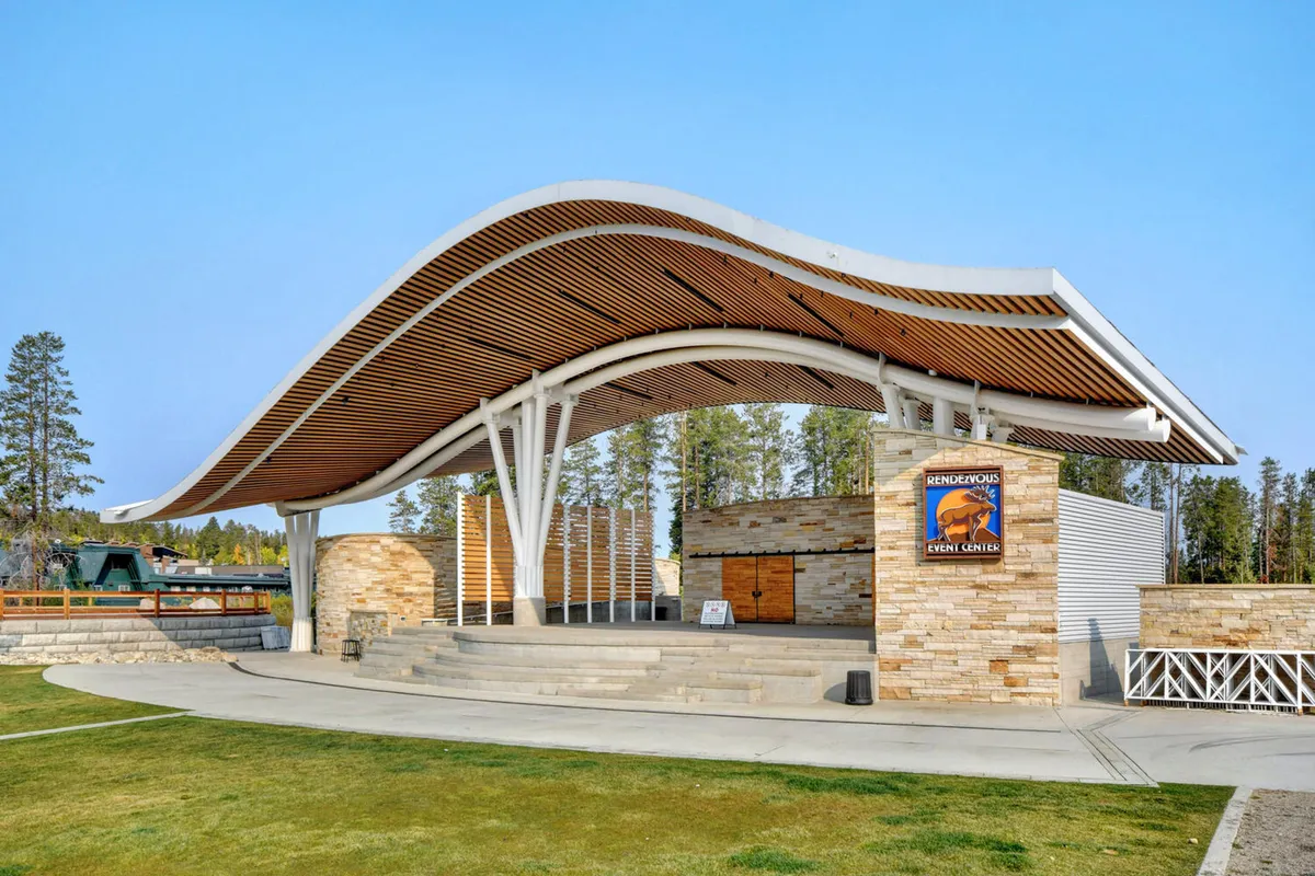 An open-air stage with a distinctive curved roof and stone walls sits at the heart of downtown, surrounded by festival seating and gathering spaces. The area is lively, designed for concerts and community events, capturing the vibrant entertainment scene.