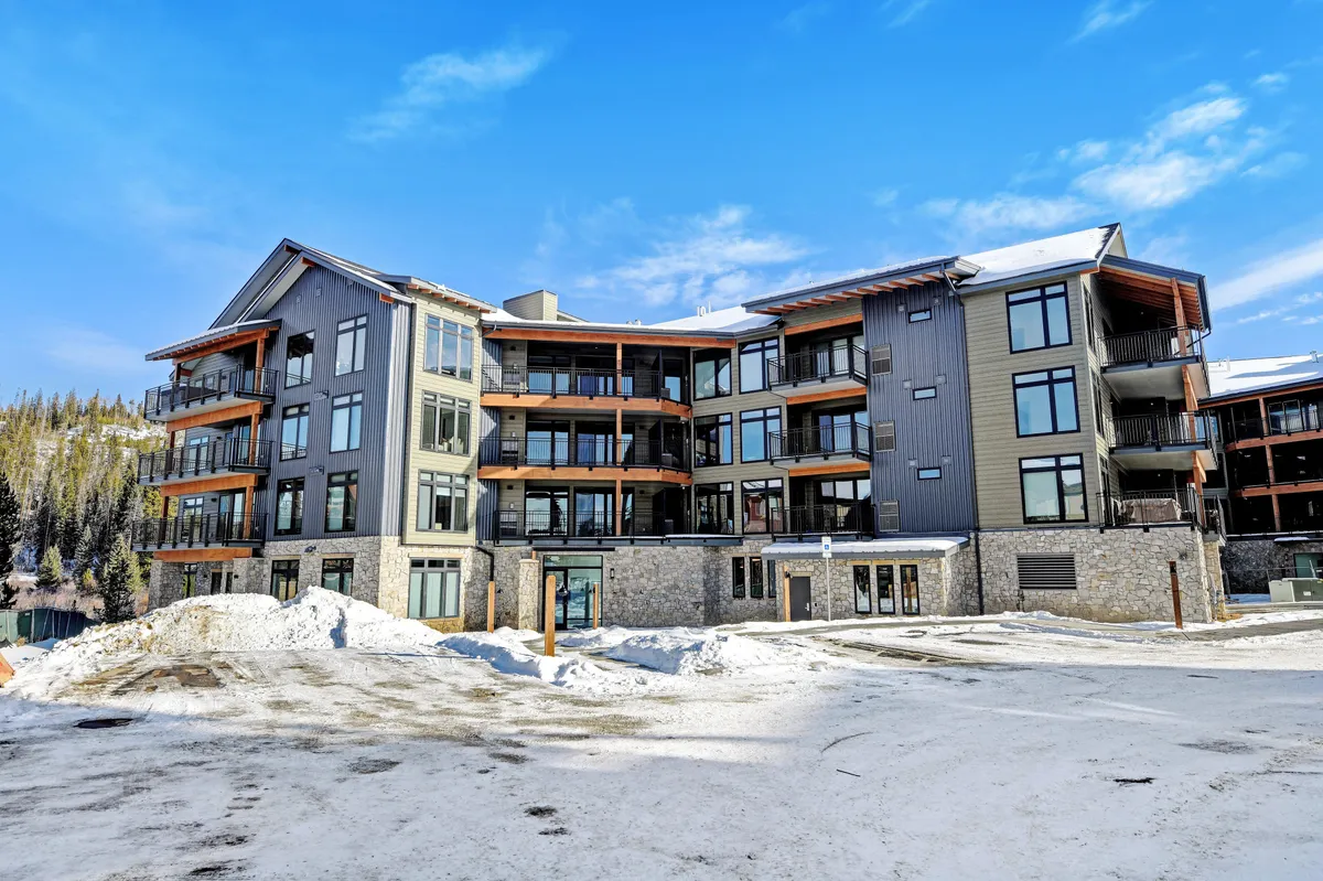 A modern luxury condo exterior with large windows and snow-covered surroundings. It conveys a sense of cozy sophistication, with hints of both adventure and relaxation, set perfectly within the winter mountain landscape just steps from downtown attractions.